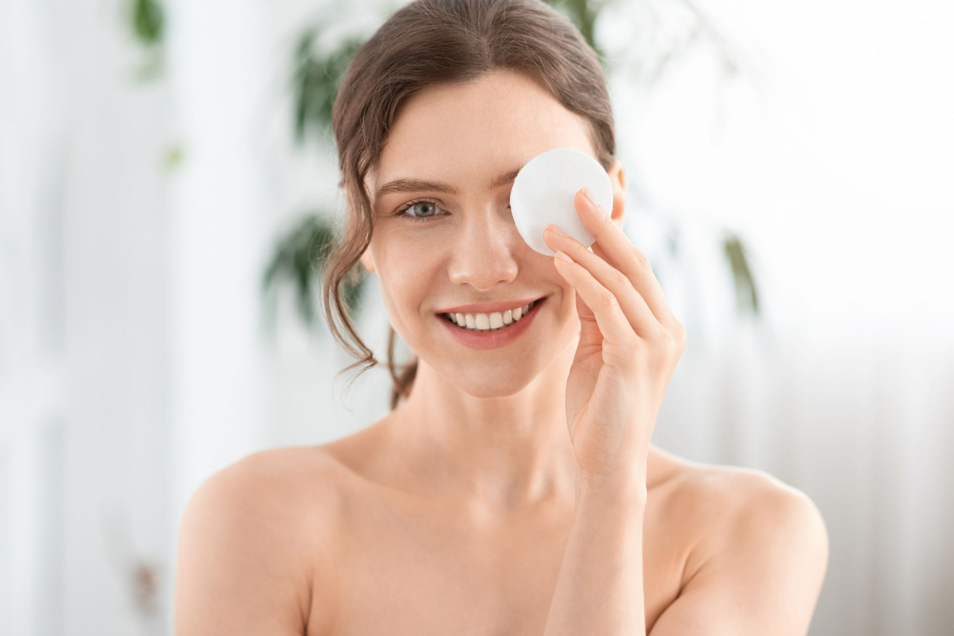 Joyful Young Lady Removing Makeup From Her Eyes, Covering One Eye With Cotton Pad And Smiling At Cam