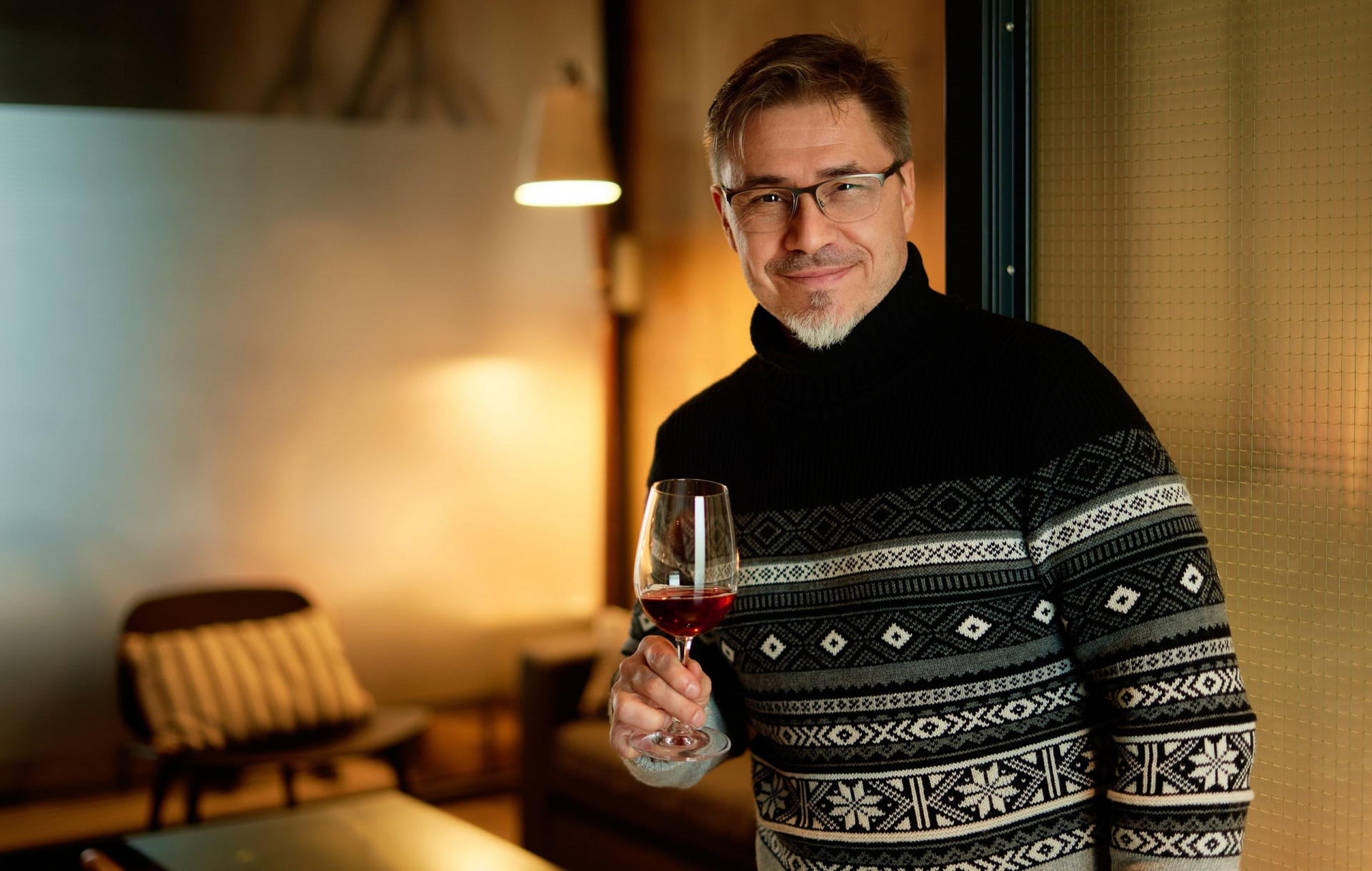 Happy man drinking wine in winter holding wine glass, smiling. Wine tasting at home. Portrait of mat
