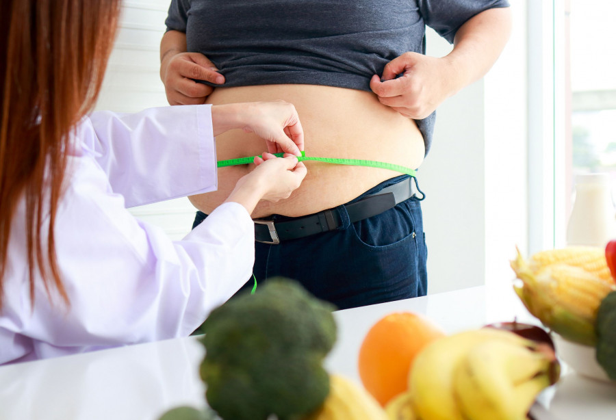 A Female Doctor Or Nutritionist Checks The Health Of An Obese Person Using A Tape Measure Around The