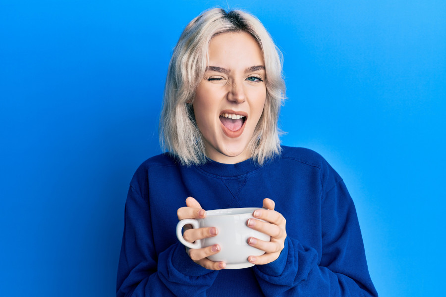 blonde girl drinking a cup of coffee winking