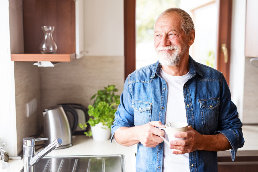 Happy Senior Man In The Kitchen Holding A Cup Of Coffee