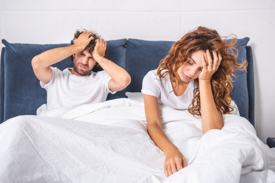 Young Couple Sitting On Bed And Suffering From Headache