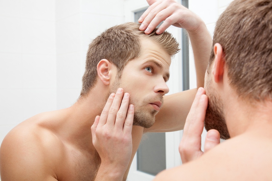 Man standing in front of mirror worrying about hair loss
