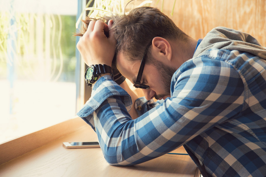Depressed Man Sitting At Table With Mobile Phone