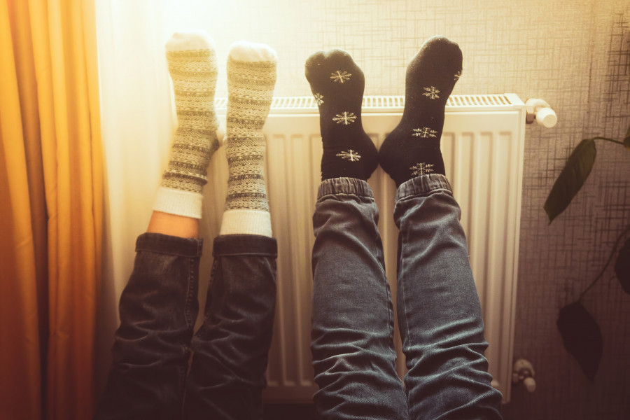 Couple Hold Legs Up Heating Feet In Cold Home Indoors On Radiator
