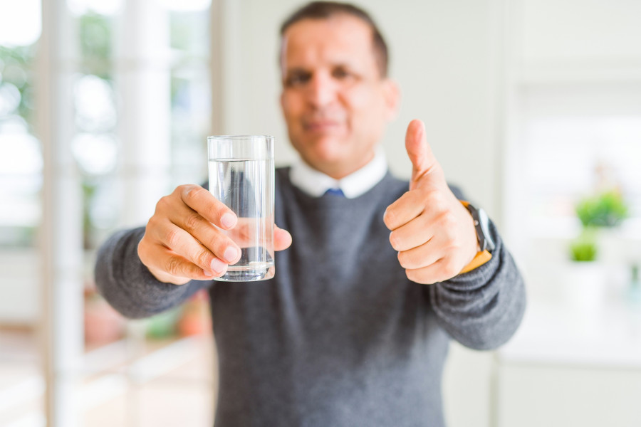 Middle age man drinking glass of water at home happy