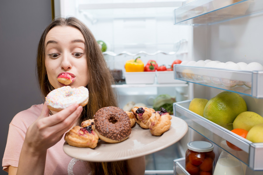 woman eating sweet donuts near the refrigerator
