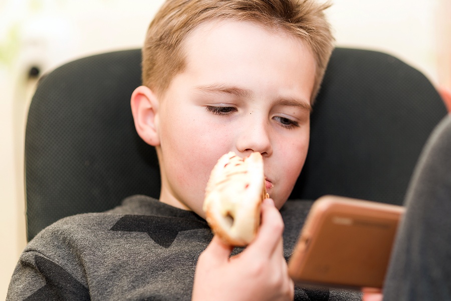 Boy Eating A Hot Dog While Playing With The Smartphone