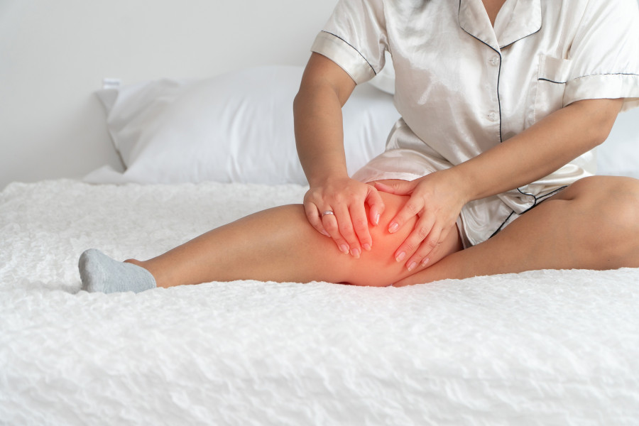 woman sitting on the bed and catching the knees because of the pain