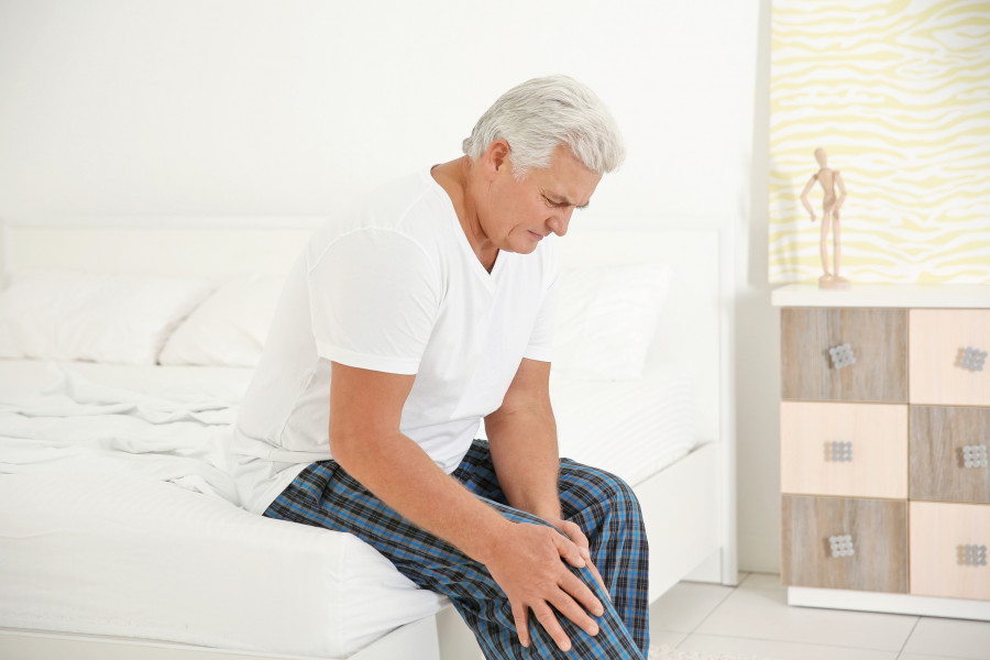 man suffering from knee pain in bedroom