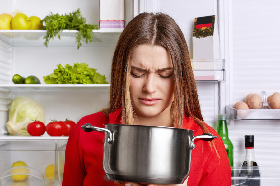 Woman with stinking food in home kitchen