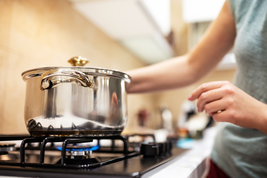 Woman Dinner in steel saucepan, standing it on gas-stove