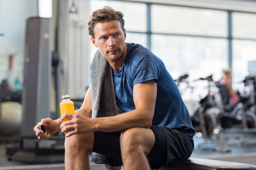 man holding bottle of fresh orange juice in gym