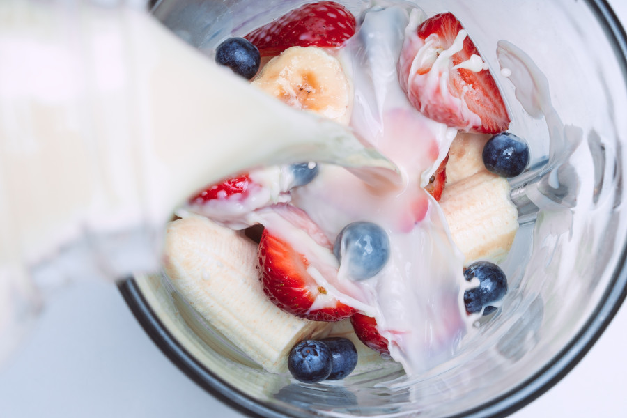 Pouring milk in a blender with fruits