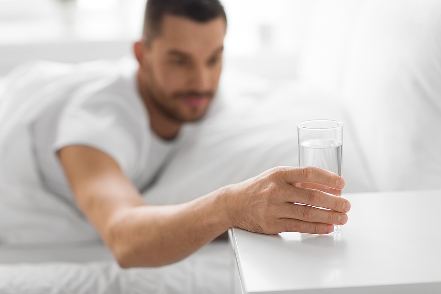 man reaching to glass of water on bedside table