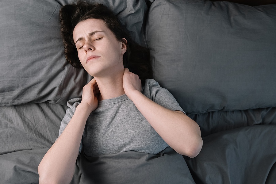 woman lying in bed in morning feels pain in neck