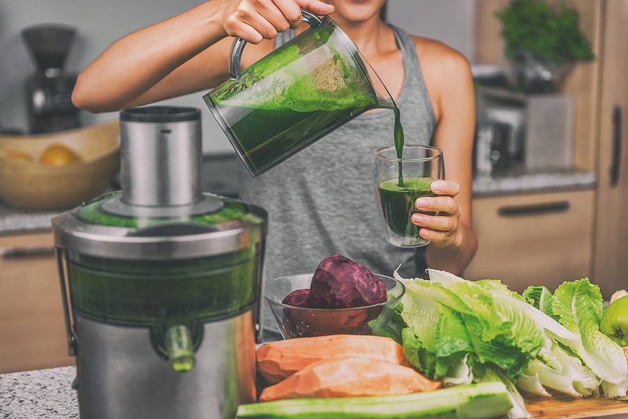 Woman juicing making green juice with juice machine